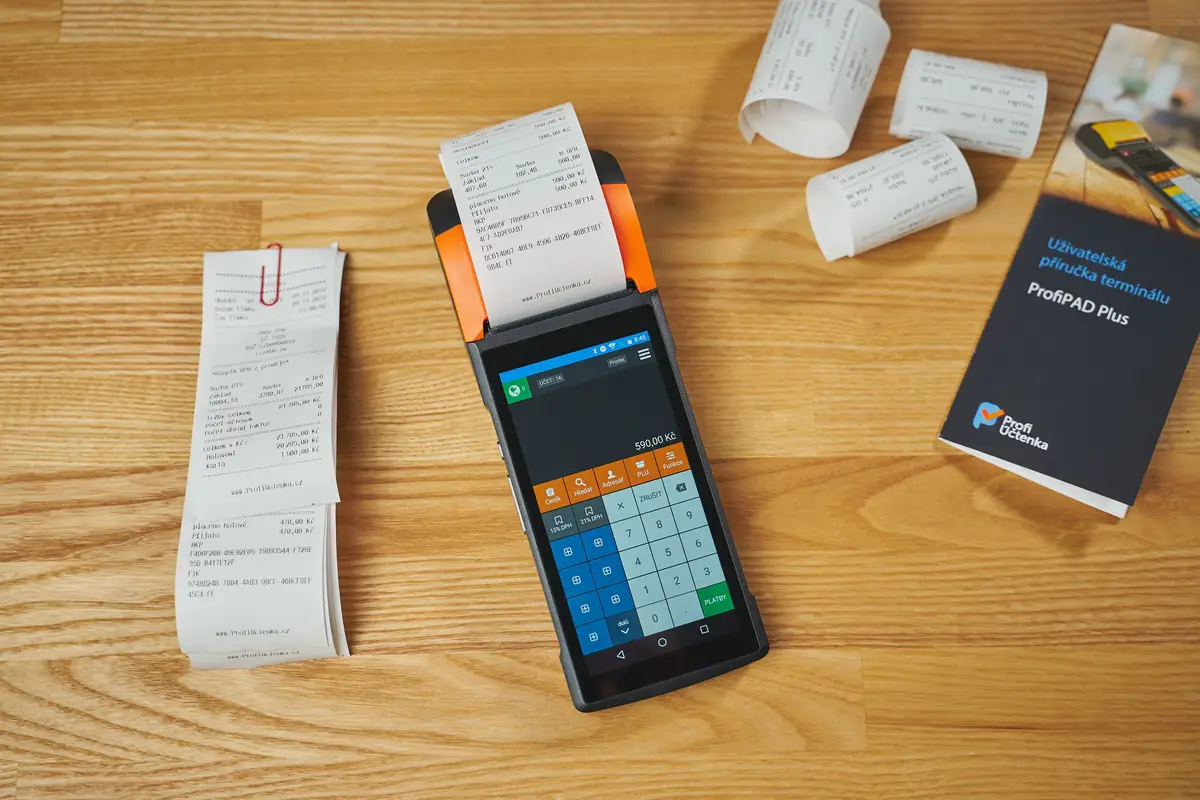 A payment terminal and a stack of printed receipts on a wooden desk.